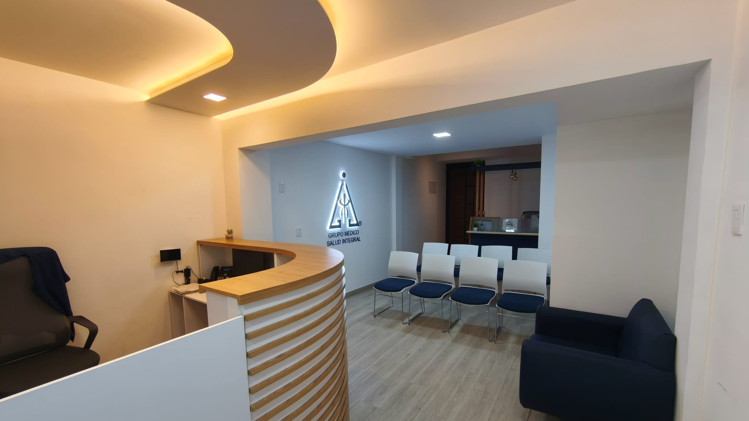 Recepción de MESAI: barra curva de madera, logo iluminado y la sala de espera al fondo