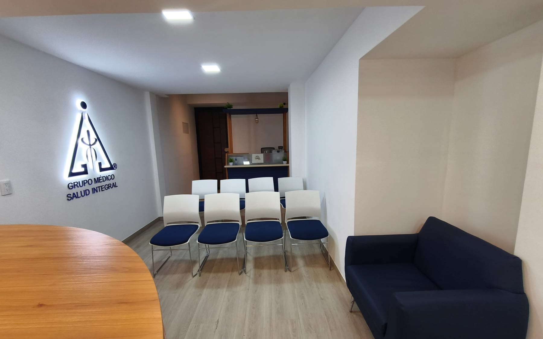 Sala de espera de MESAI con sillas blancas, sillón azul y el logo iluminado en el muro